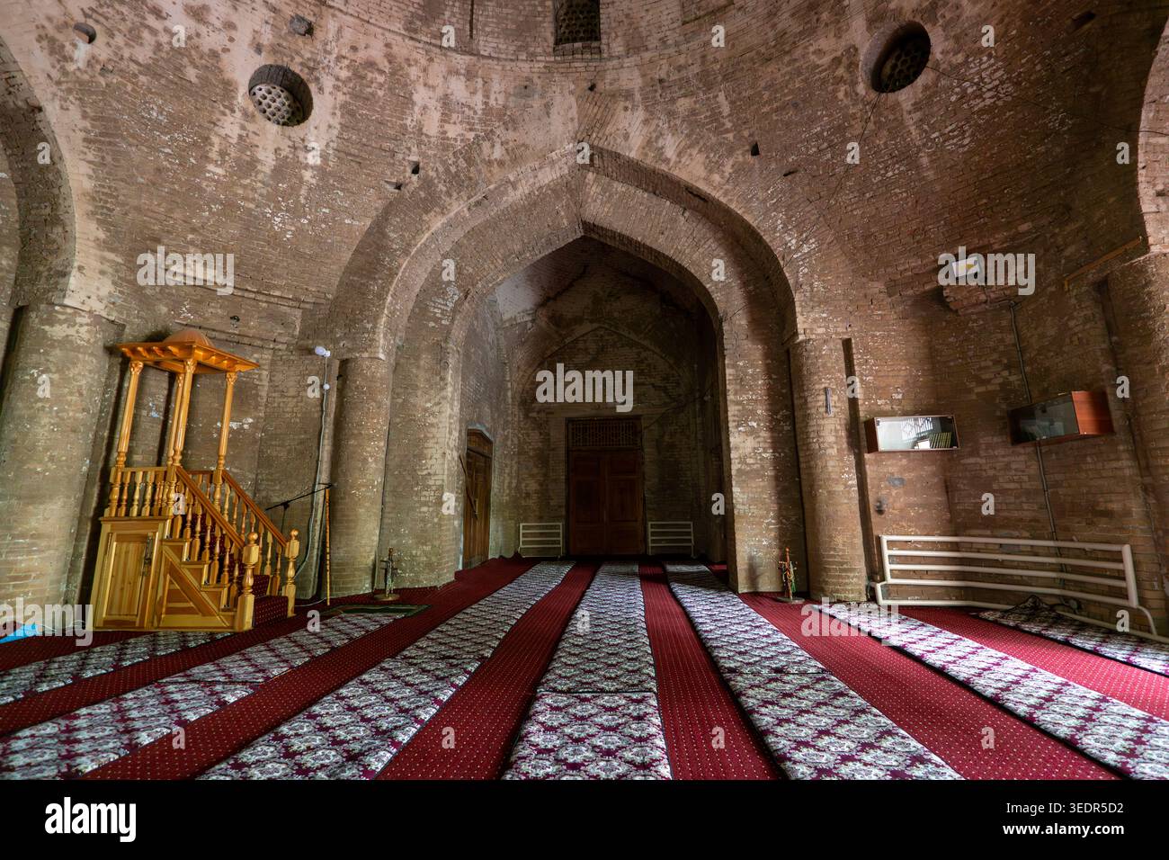 Blick von innen auf eine alte leere Steinmauermoschee mit Teppichen auf dem Boden. Stockfoto