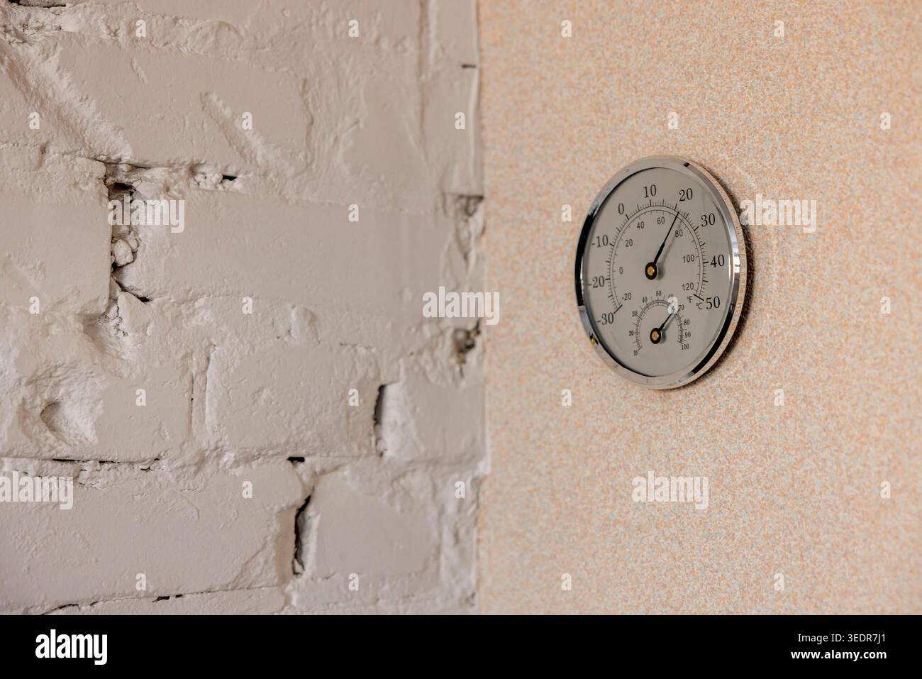 Analoges Thermometer und Hygrometer, die an einer Innenwand montiert sind, messen Temperatur und Luftfeuchtigkeit, runder Metall-Klimamesser für die Innenumgebung Stockfoto