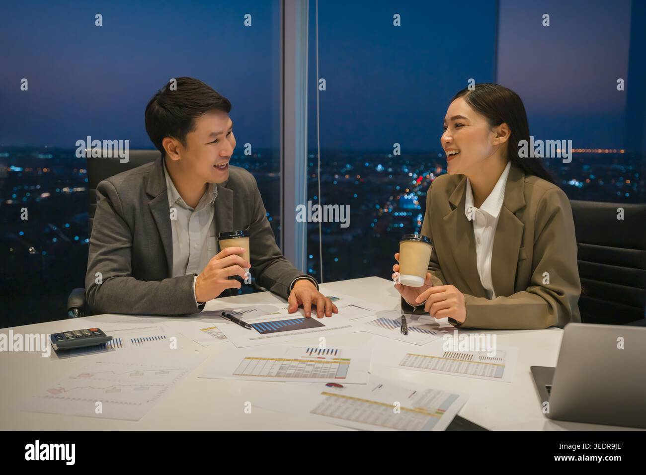 Zwei glückliche Geschäftskollegen treffen sich, führen ein zwangloses Gespräch und trinken abends Kaffee im modernen Büro Stockfoto