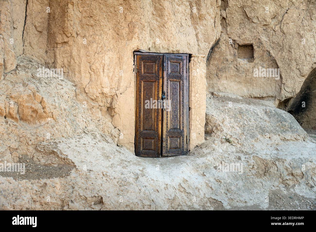 Antike Holztür, die in die Felswände eingefasst ist. Alte Eisenscharniere und Schloss. Eingang in Steinklippe gehauen. Zentralasiatische Bergarchitektur. Stockfoto
