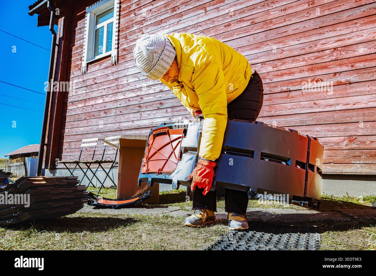 Ineinander greifende Kompostbehälter-Paneele, die von einer Frau in der Nähe des Landhauses zu einer kreisförmigen Struktur verbunden werden. Stockfoto