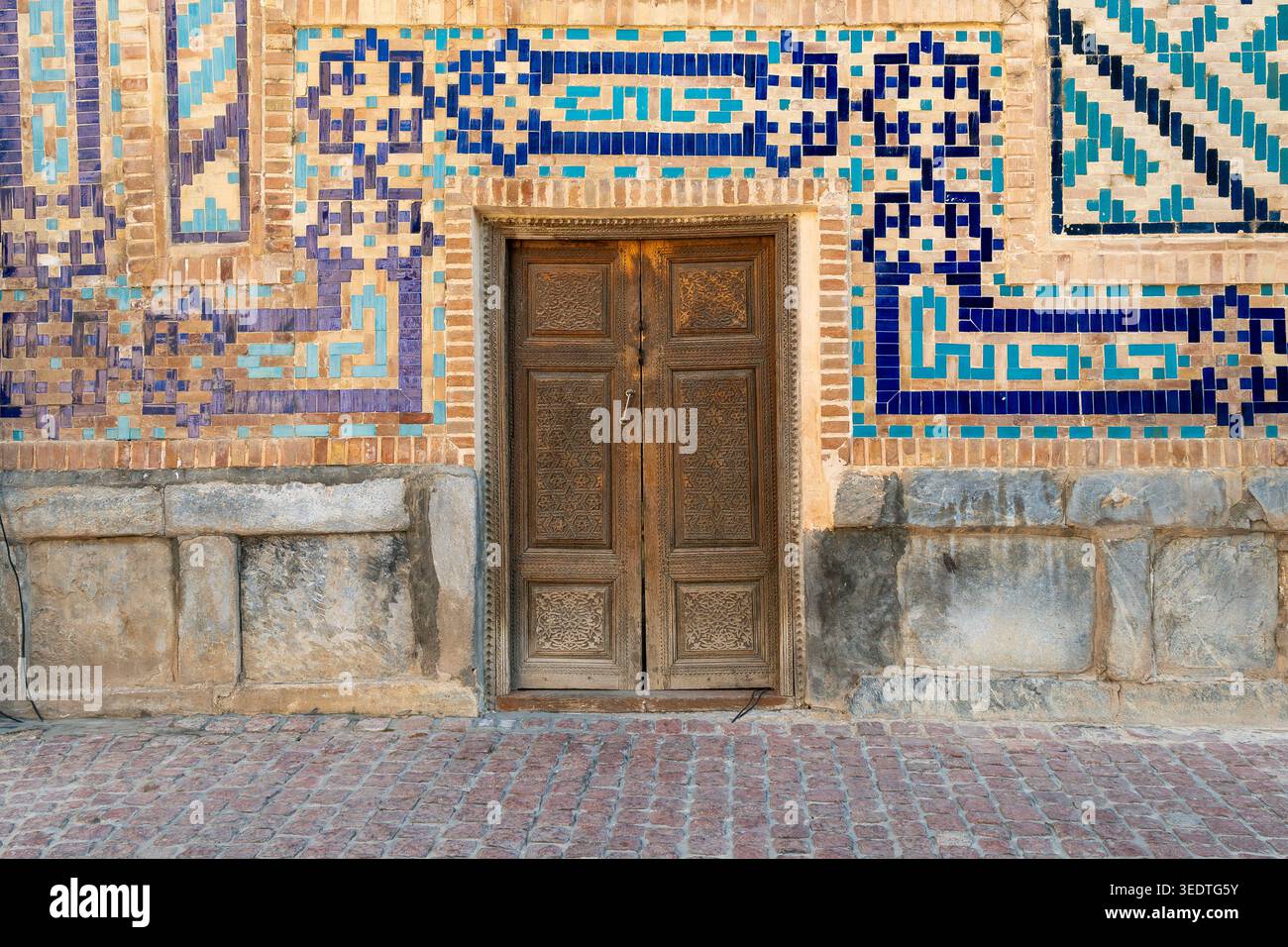 Kunstvoll geschnitzte Holztür mit traditionellen usbekischen Majolika-Fliesen in blauen und türkisfarbenen Farben. Antike architektonische Details mit geometrischen Mustern Stockfoto