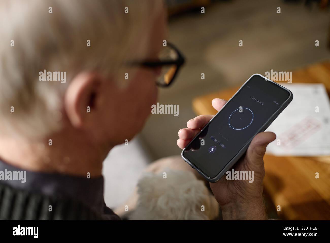 Senior-Mann, der zu Hause den Sprachassistenten des Smartphones nutzt Stockfoto