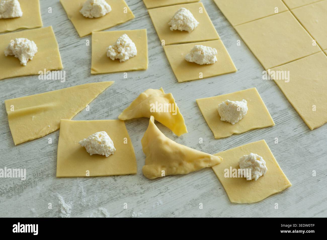 Pasta-Teig-Quadrate mit Weißkäsefüllung und gefalteten Ravioli auf Holzoberfläche. Stockfoto