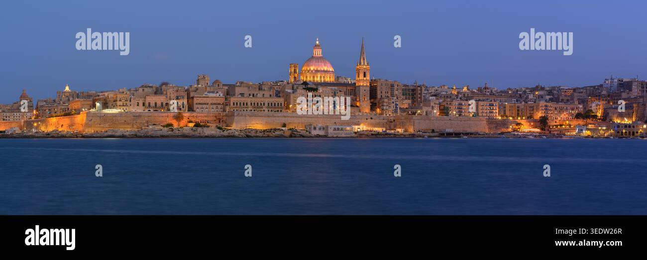 Panoramablick auf die Skyline von Valletta in der Abenddämmerung vom Hafen Sliema mit Lichtern auf der St. Pauls Kathedrale, Malta. Stockfoto