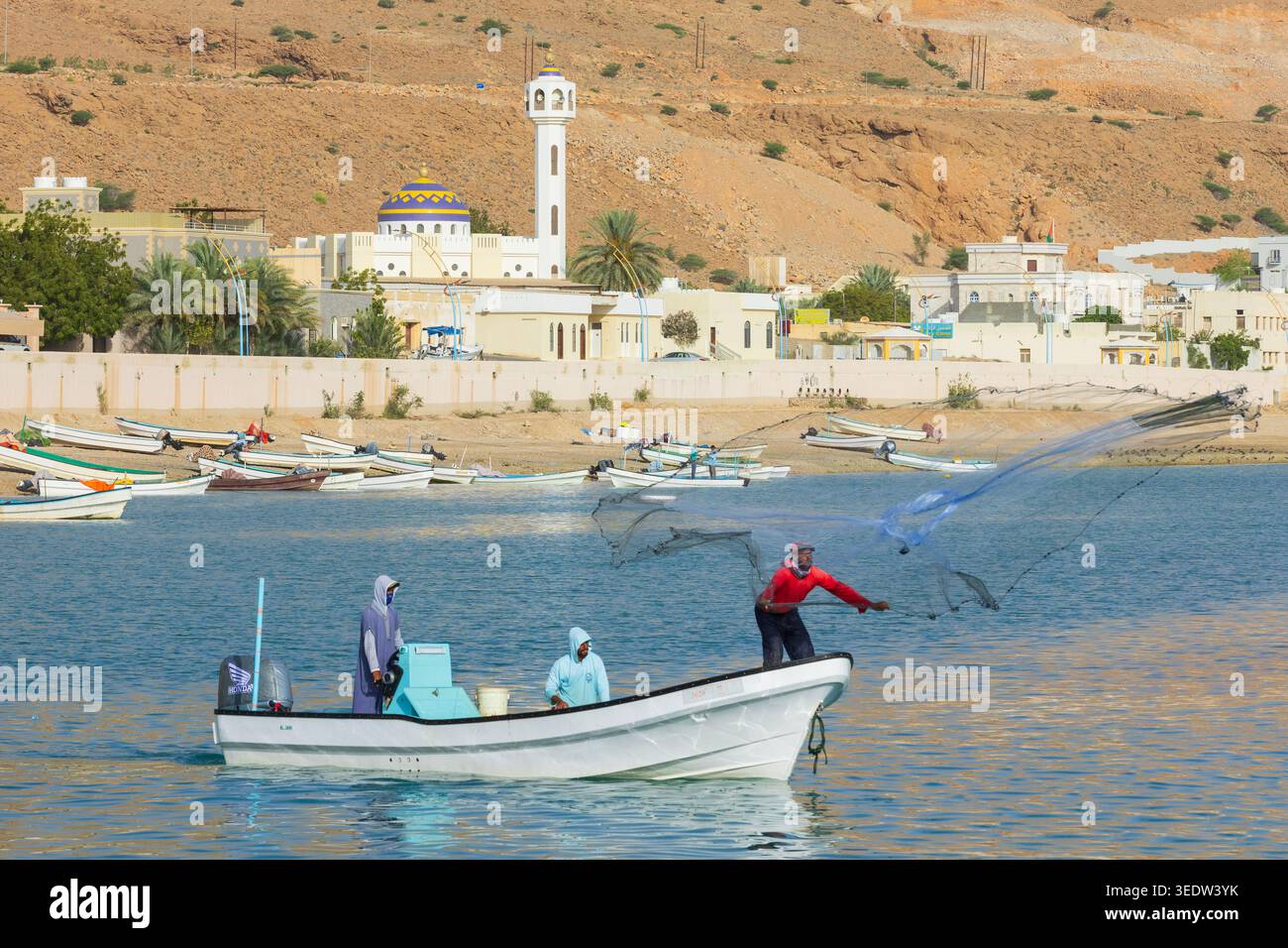 Fischer (gegossene Netze) werfen ein rundes, gewichtetes Netz ins Wasser, um im kleinen Fischerhafen Tiwi im Sultanat Oman Fische zu fangen Stockfoto