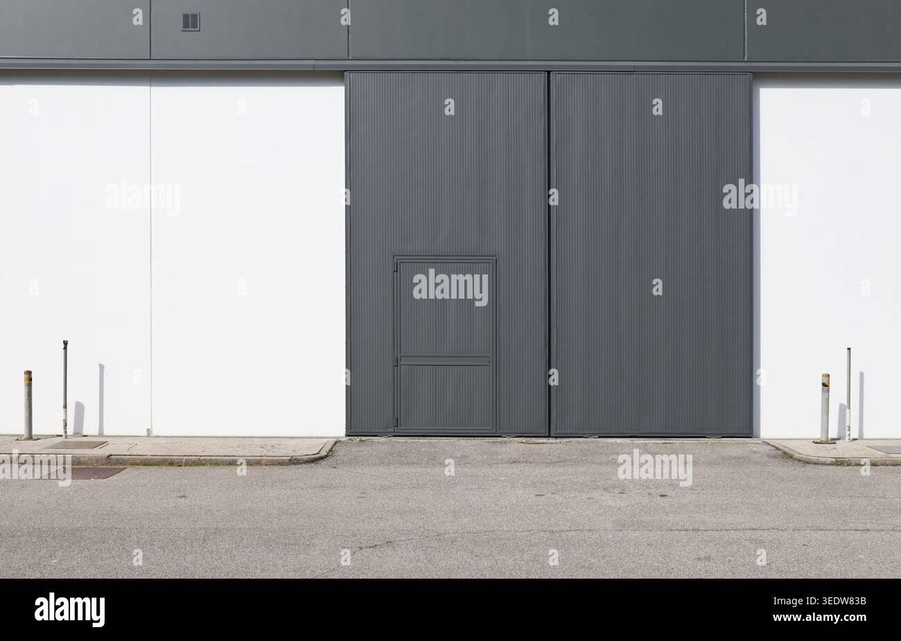 Industrietür (oder Seitenklapptür) aus dunkelgrauem Metall mit integrierter Fußgängertür. Hintergrund und Textur. Stockfoto
