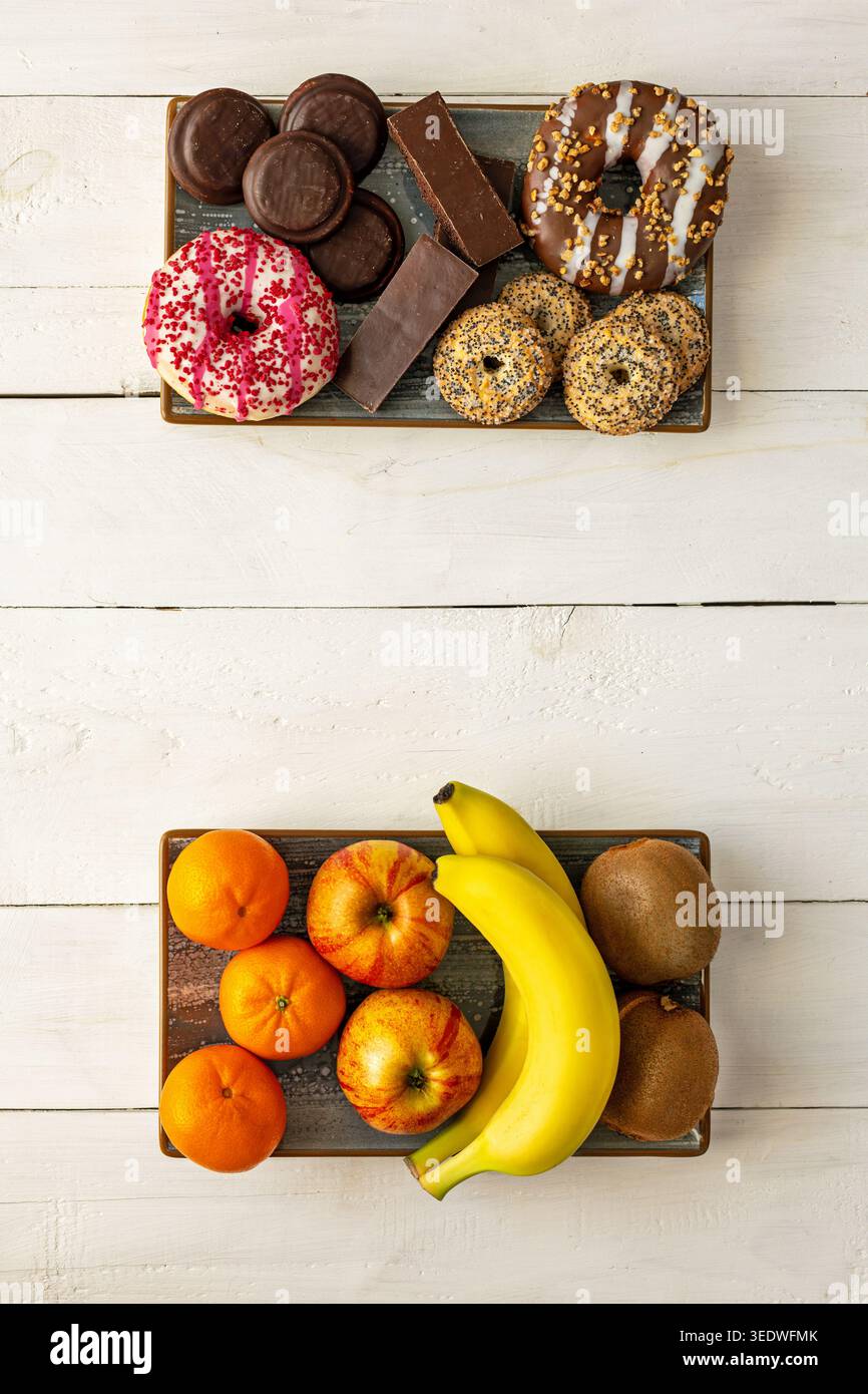 Gesunde Obstteller Versus Süße Desserts. Blick von oben auf Obst- und Dessertteller mit gesunden Snacks und Donuts, Keksen, Schokoladentafeln und Stockfoto