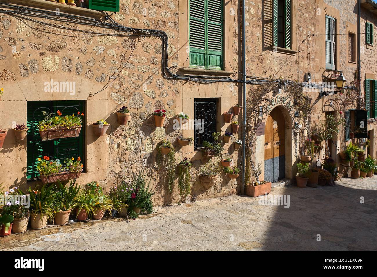 Valldemossa, Spanien - 6. Mai 2026: Malerischer Blick auf die Straße auf traditionelle Steinhäuser mit grünen Fensterläden und zahlreichen bunten Blumentöpfen, die an der hängen Stockfoto