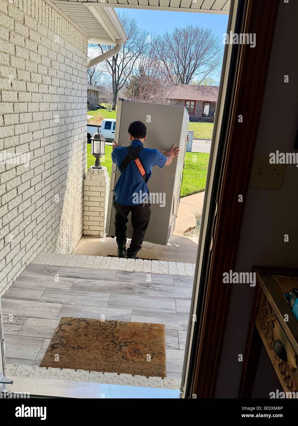 Ein Arbeiter entfernt einen alten Kühlschrank durch die Eingangstür eines Wohnhauses in Wichita, Kansas, USA. - Smartphone-aufgenommenes Stockfoto