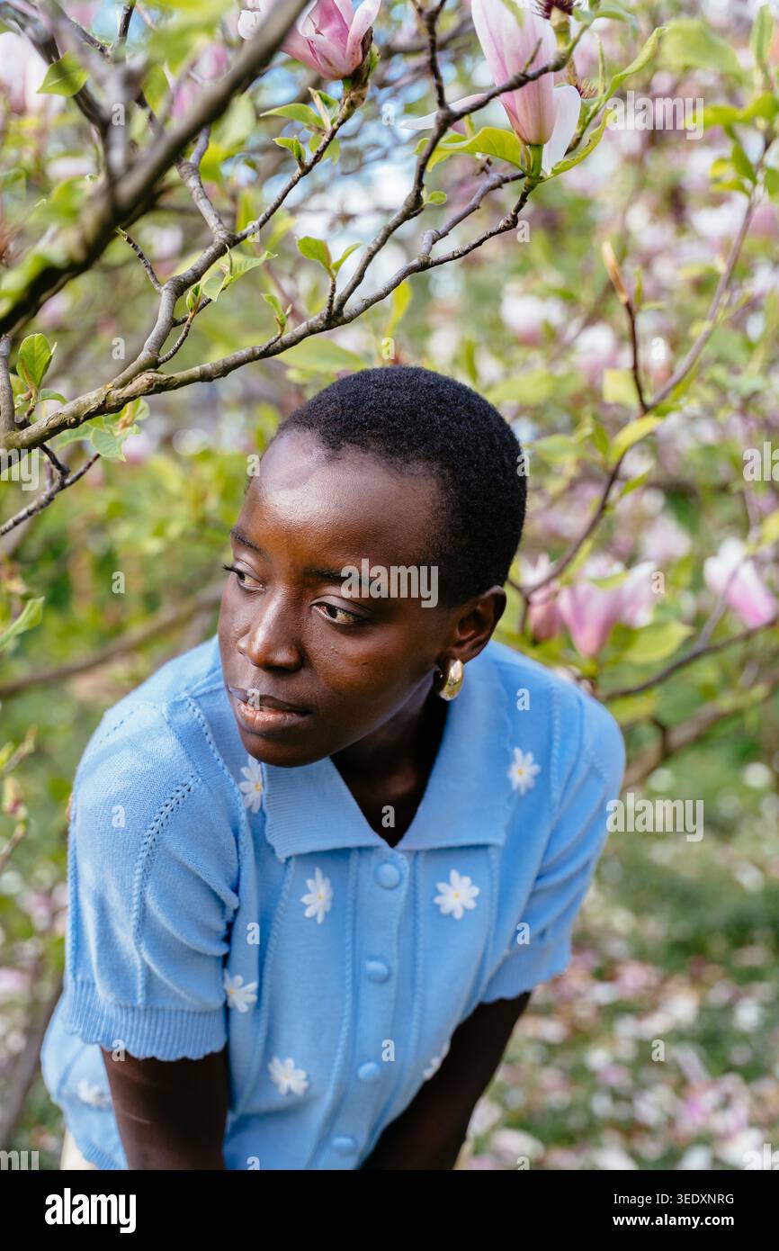Nachdenkliche Afrikanerin reflektiert im Frühlingsgarten für psychologisches Wohlbefinden. Stockfoto