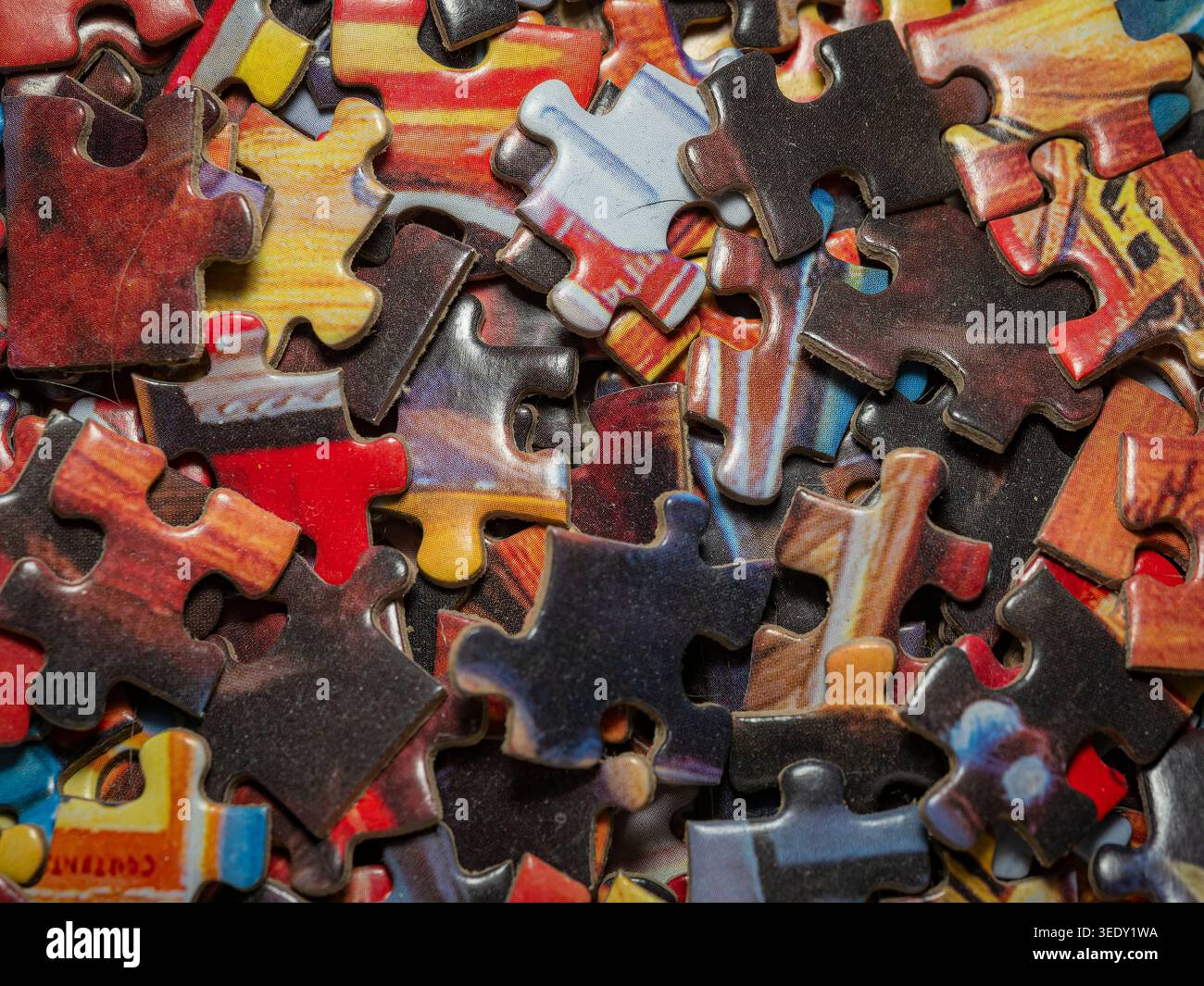 Top-Down-Makroansicht eines verstreuten Stapels von mehrfarbigen Puzzleteilen mit komplizierten Details und Texturen in einem unordentlichen Arrangement Stockfoto