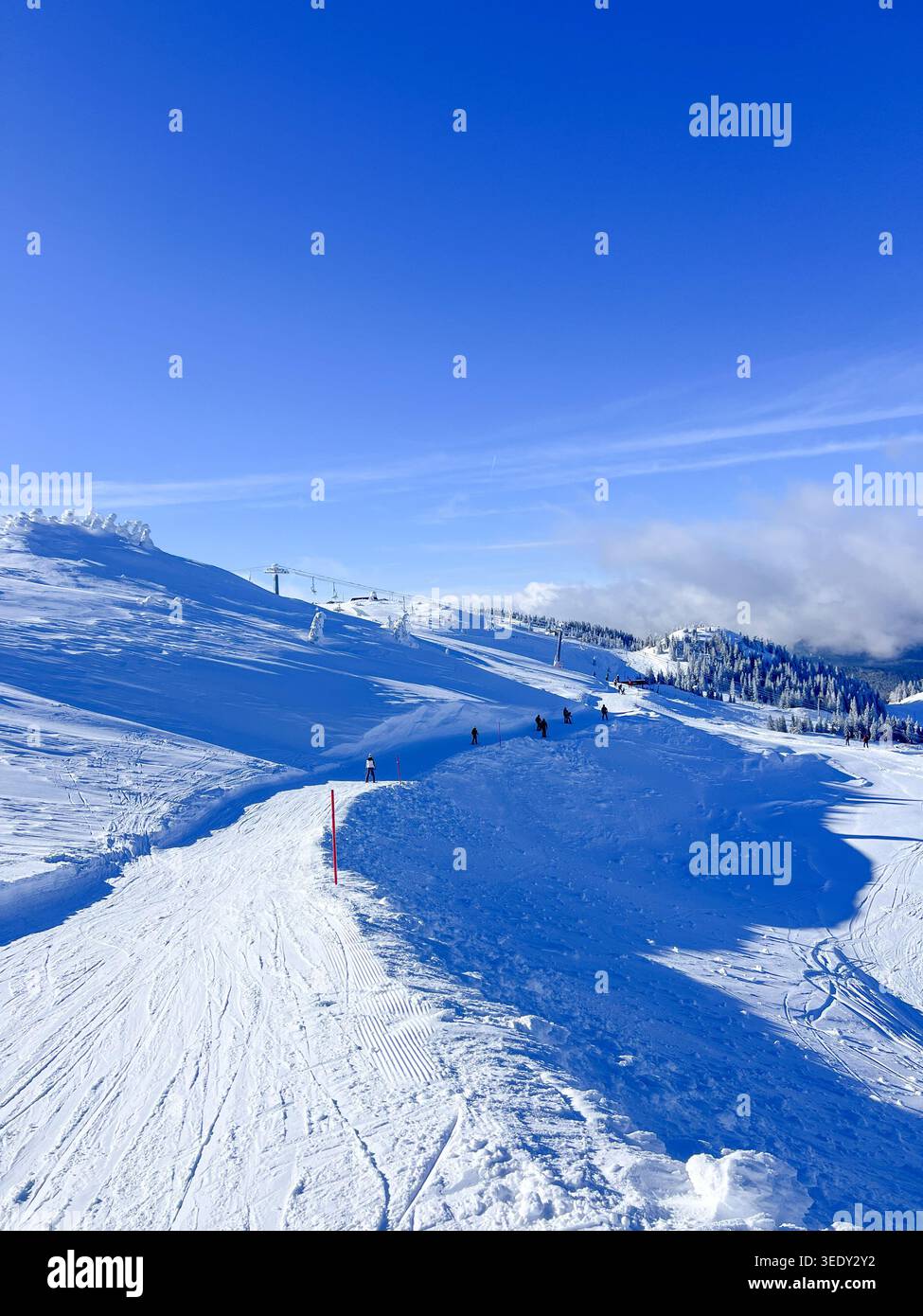 Schneebedeckte Skipiste auf dem Berg Jahorina mit Skifahrern, blauem Himmel und Winterlandschaft in Bosnien und Herzegowina. - Smartphone-aufgenommenes Stockfoto