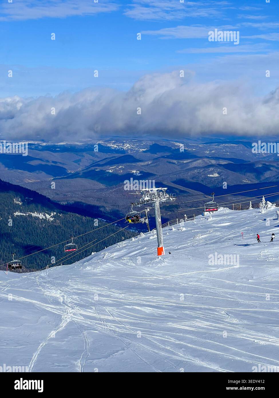 Verschneite Skipisten und Sessellift auf dem Jahorina Berg mit dramatischen Wolken und Panoramablick auf die Winterlandschaft. - Smartphone-aufgenommenes Stockfoto
