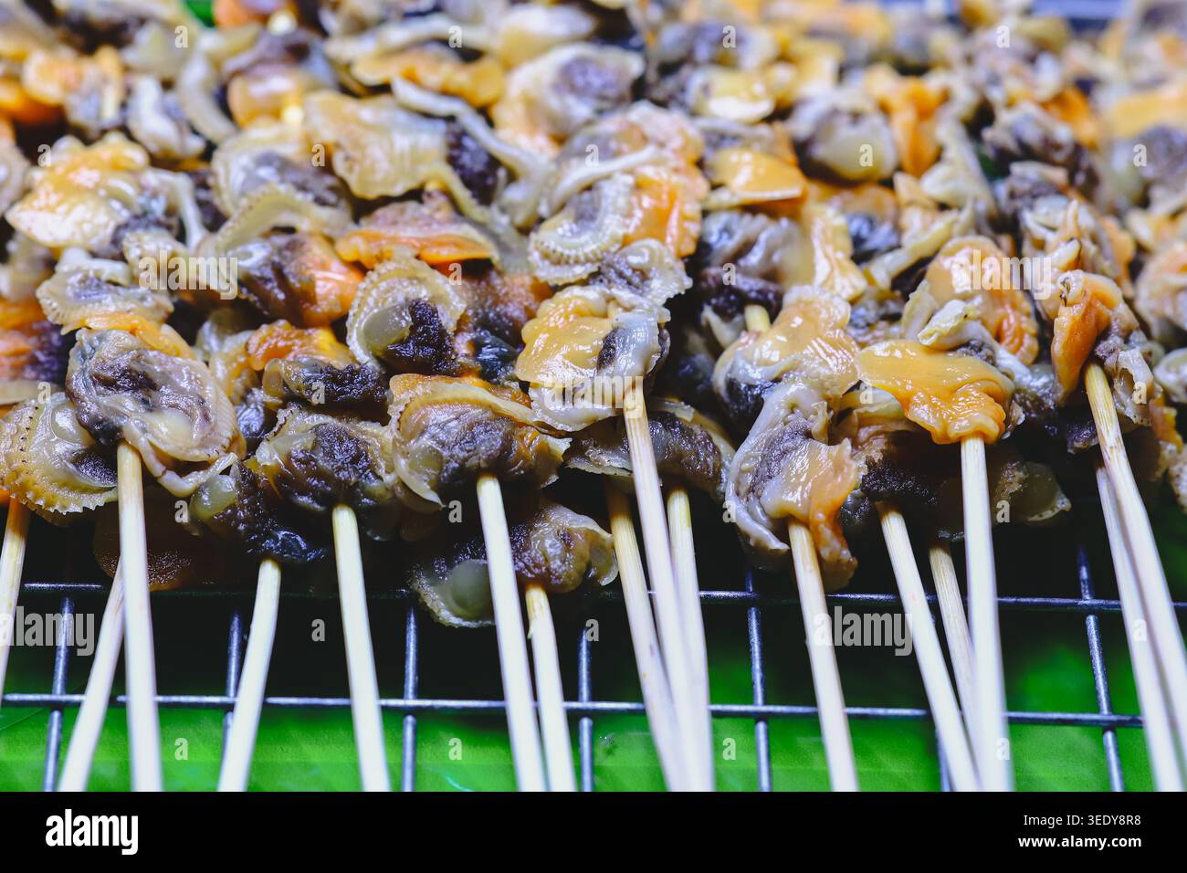 Makroansicht gegrillter Blutmuschelspieße an einem lokalen Marktstand. Authentisches thailändisches Street Food, das regionale Meeresfrüchte-Kochkultur repräsentiert. Stockfoto