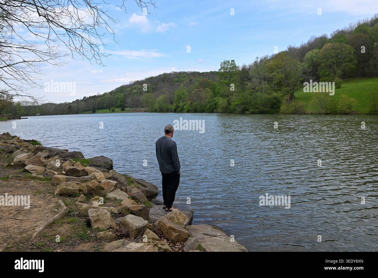 Mann, der auf dem Ufer des Sees steht, mit Blick auf grüne Hügel und grünes Gras mit großen Felsen und Schlammquellen in pennsylvania Stockfoto