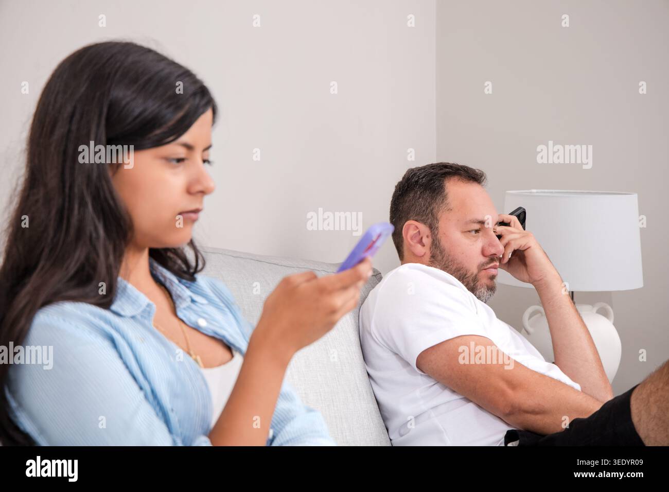 Teenager und Vater ignorieren sich gegenseitig, während sie auf ihren Mobiltelefonen surfen. Eine Szene digitaler Ablenkung und fehlender Kommunikation in den Lebenden Stockfoto