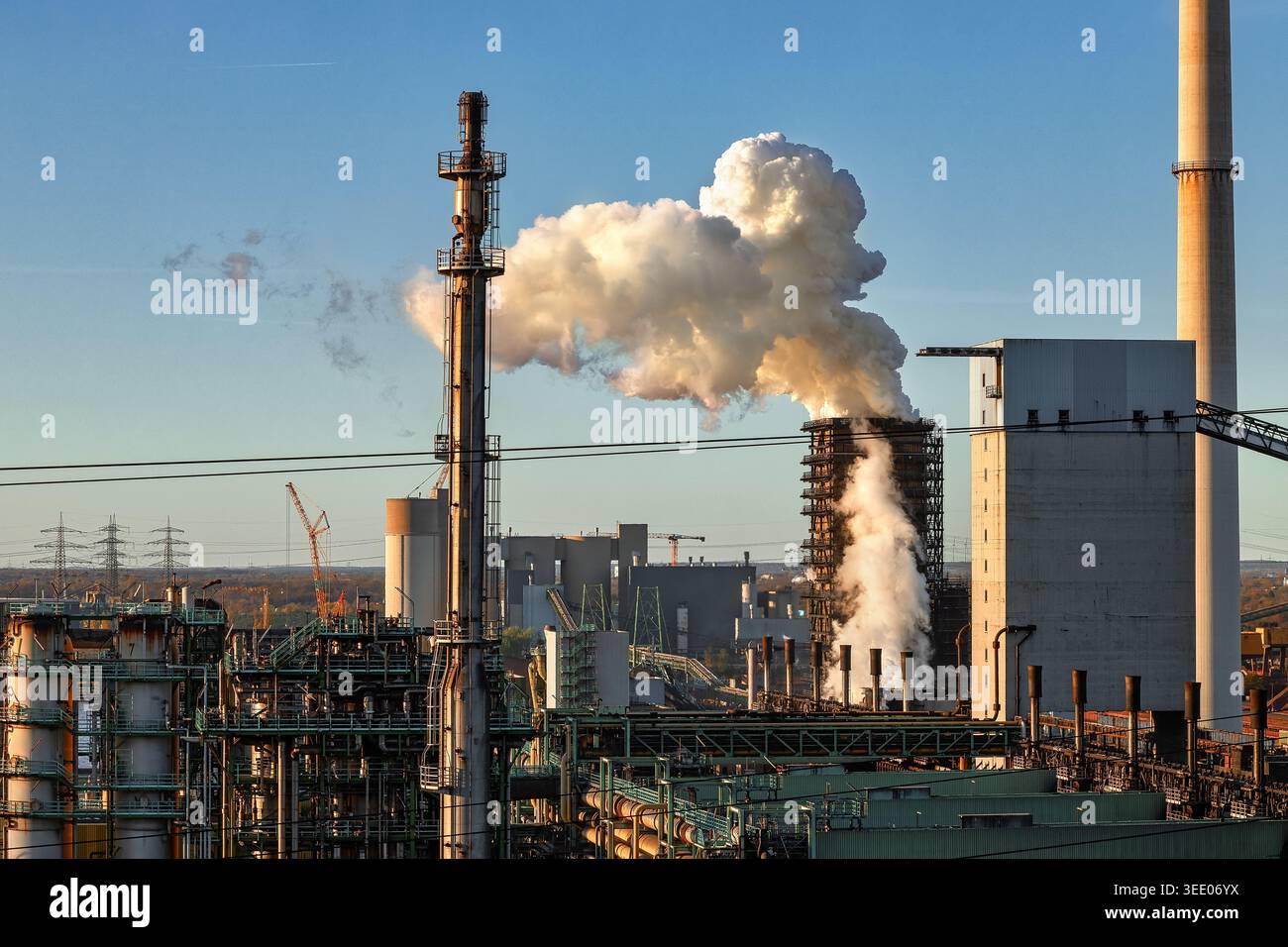 Blick auf eine Industrieanlage mit dickem weißem Rauch, der aus einem Schornsteinstapel bei Sonnenuntergang in Duisburg, Nordrhein-Westfalen, aufsteigt Stockfoto
