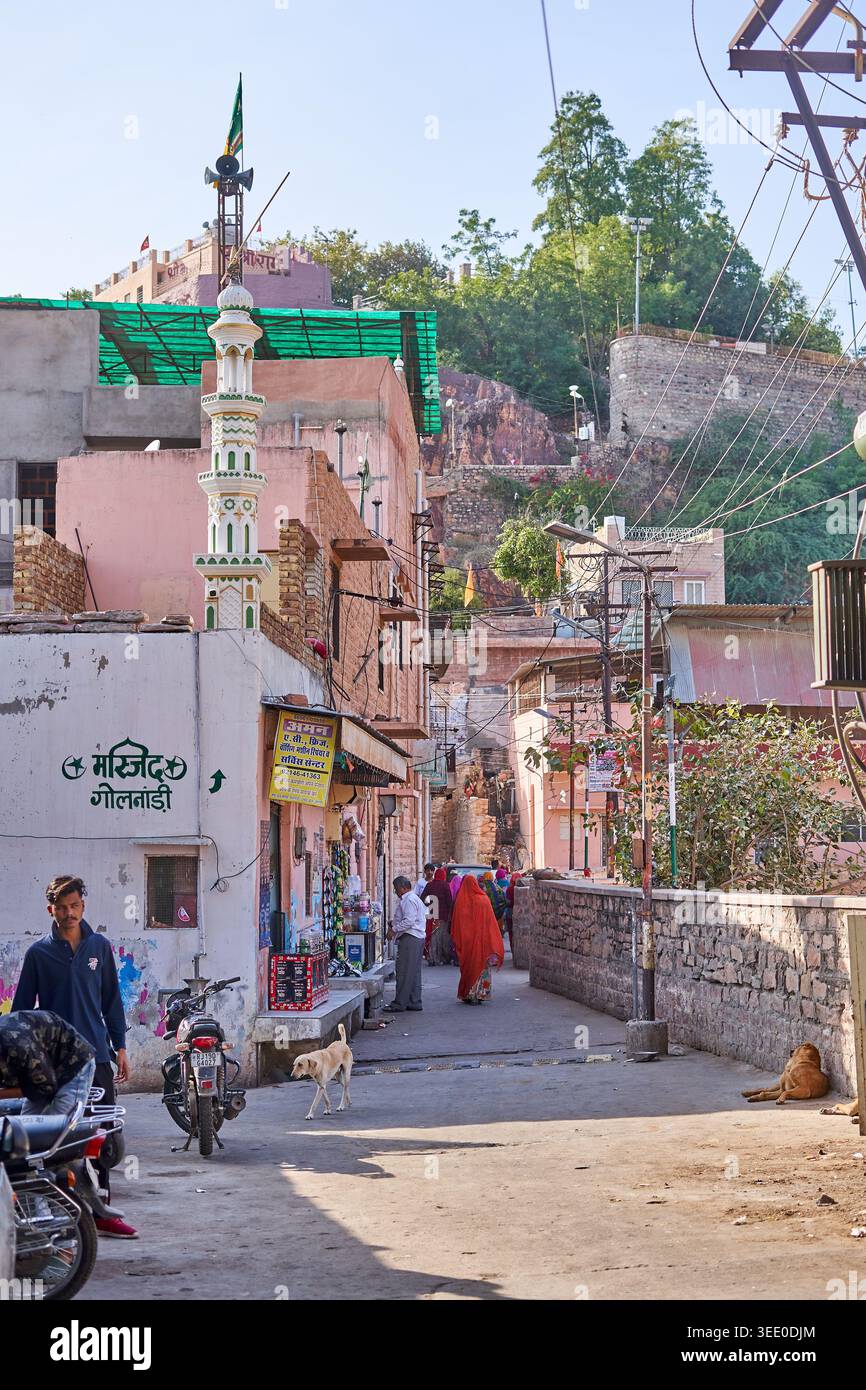 Eine schmale Straße in der Altstadt von Jodhpur, Rajasthan, Indien, mit dem imposanten Mehrangarh-Fort, das auf dem felsigen Hügel im Hintergrund zu sehen ist. Die Stockfoto