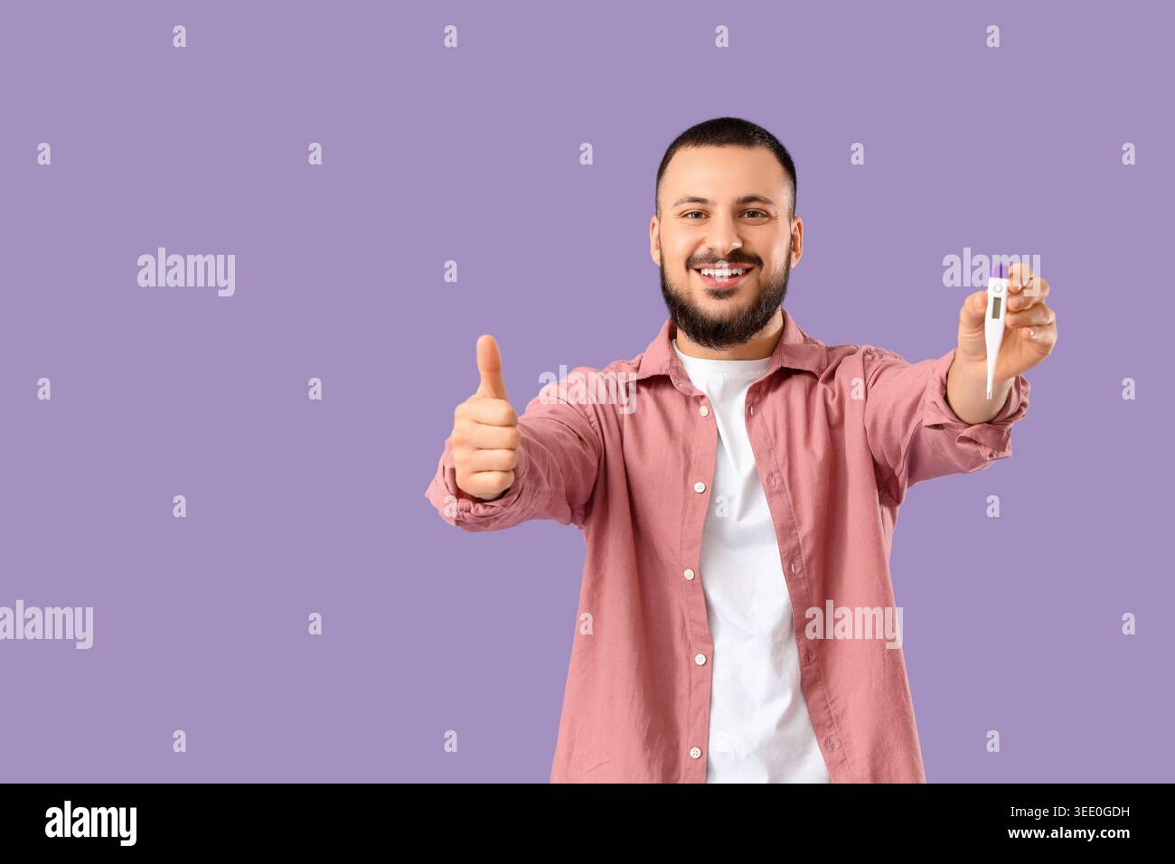 Schöner junger Mann mit Thermometer, das die Daumen-nach-oben-Geste auf lilafarbenem Hintergrund zeigt Stockfoto