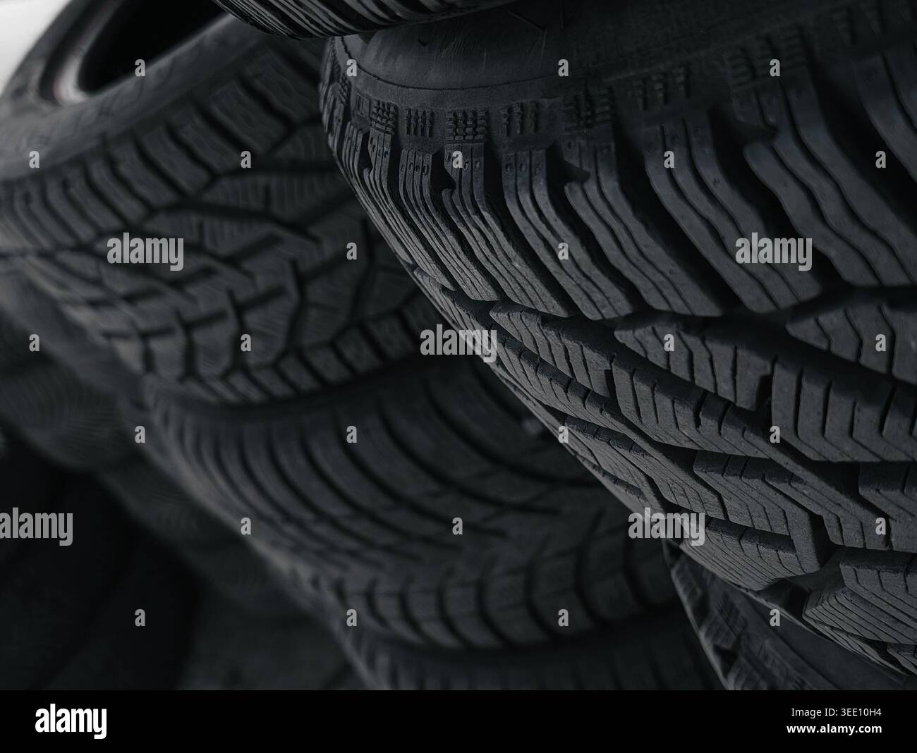 Nahaufnahme des Reifenprofils im Winter. Gebrauchte Winterreifen in einer dunklen Werkstatt stapeln – selektives Fokusbild zur Betonung der Gummistruktur mit Lamellen. Stockfoto