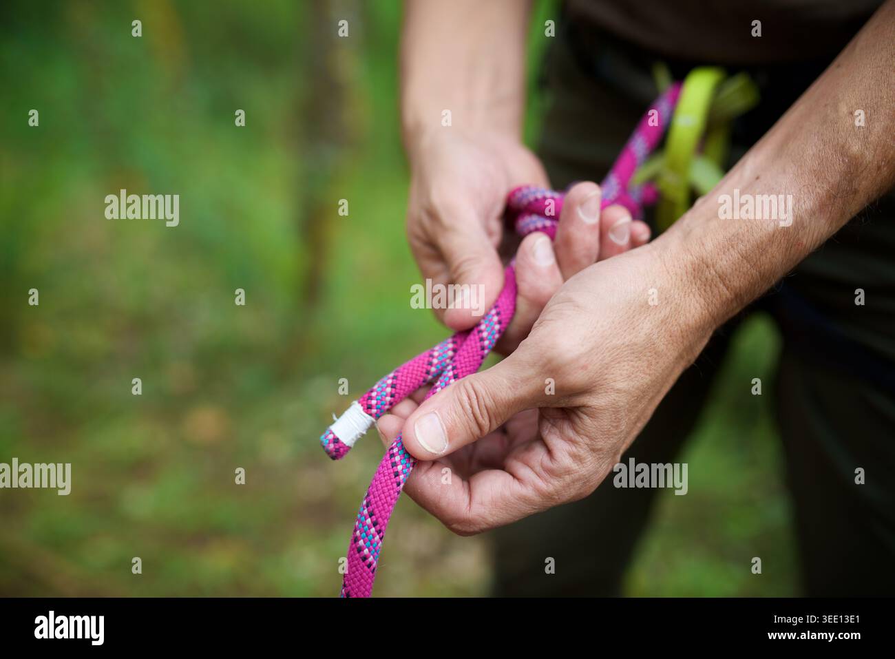 Nahaufnahme eines Kletterers, der das Kletterseil an seinem Klettergurt knüpft Stockfoto