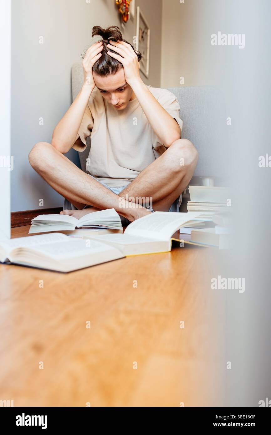 Gestresster Jugendlicher, der beim Studium mit offenen Büchern den Kopf hält Stockfoto