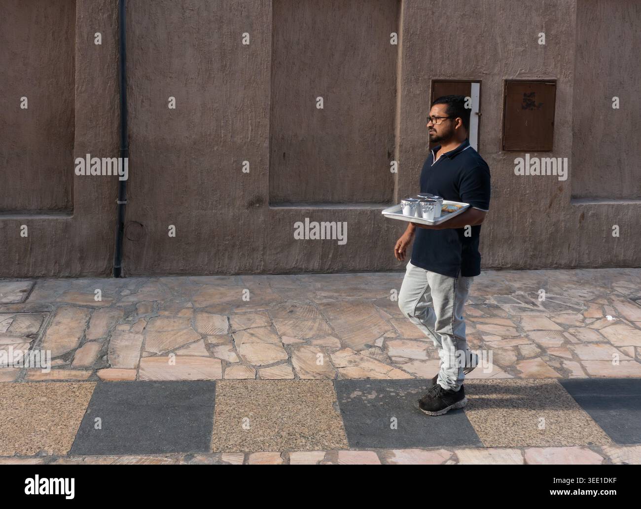 Ein Mann, der die Gasse hinunterläuft und Kaffeetassen auf einem Tablett in Bur Dubai, Dubai, den Vereinigten Arabischen Emiraten trägt. Stockfoto