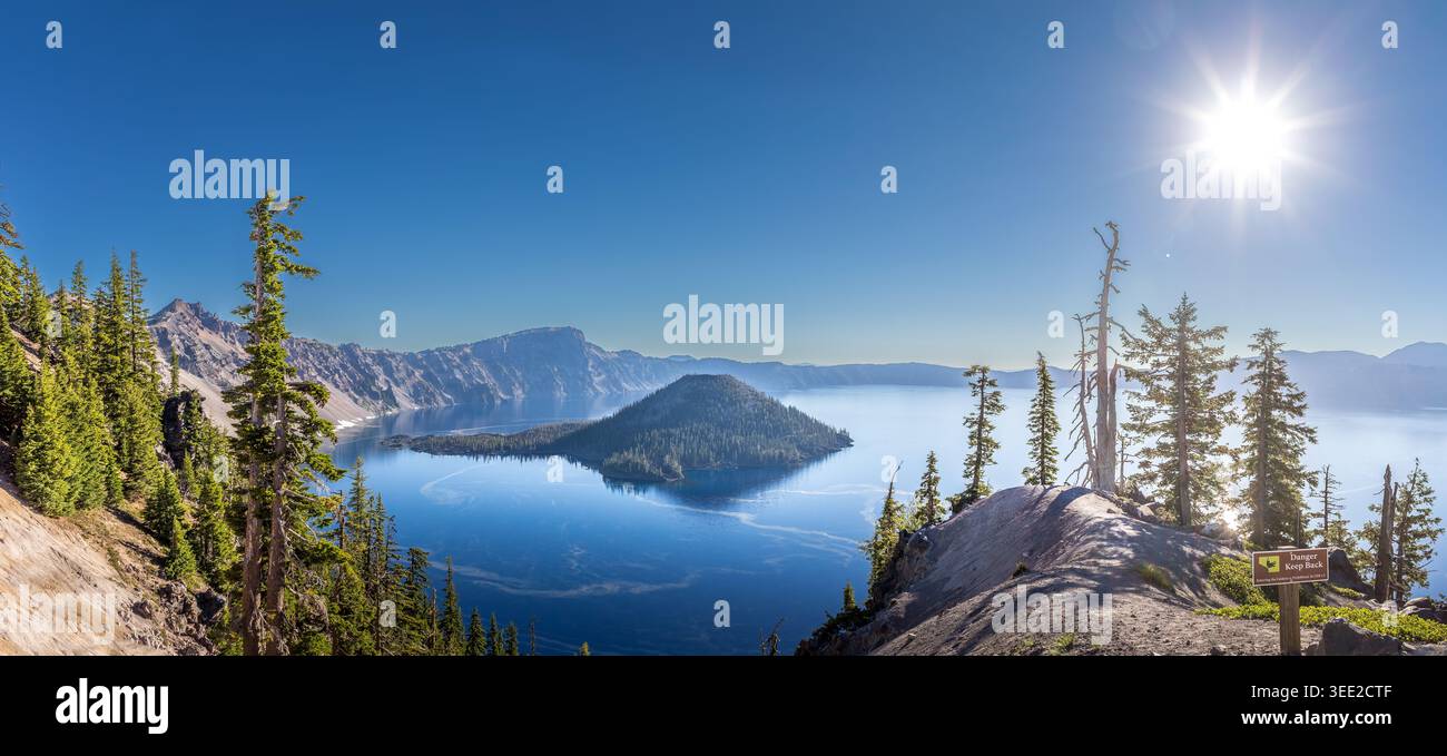 Tiefblauer Crater Lake umgeben von steilen vulkanischen Kaldera-Klippen mit Wizard Island unter einem klaren Himmel in Oregon Stockfoto