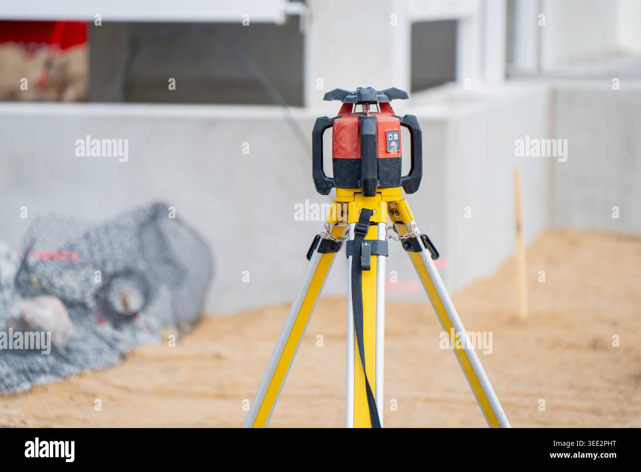 Professionelles rotierendes Laser-Niveaugerät, montiert auf einem gelben Stativ auf einer industriellen Baustelle zur präzisen Vermessung von Betonfundamenten Stockfoto
