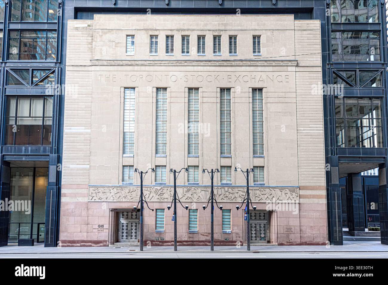 Vorderansicht der Toronto Stock Exchange Fassade mit gravierten Schildern, vertikalen Fenstern und symmetrischem Steindesign, das von Glasgebäuden eingerahmt wird. Stockfoto