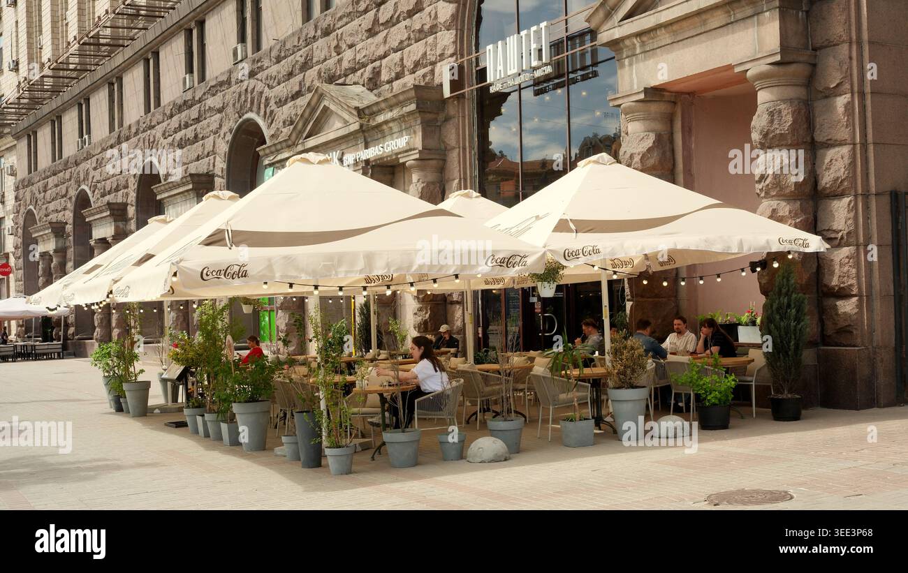 Besucher genießen Drinks unter großen Sonnenschirmen in einem lebhaften Stadtcafé. Chreshtschatjk, Kiew, Ukraine, 8. Mai 2026 Stockfoto