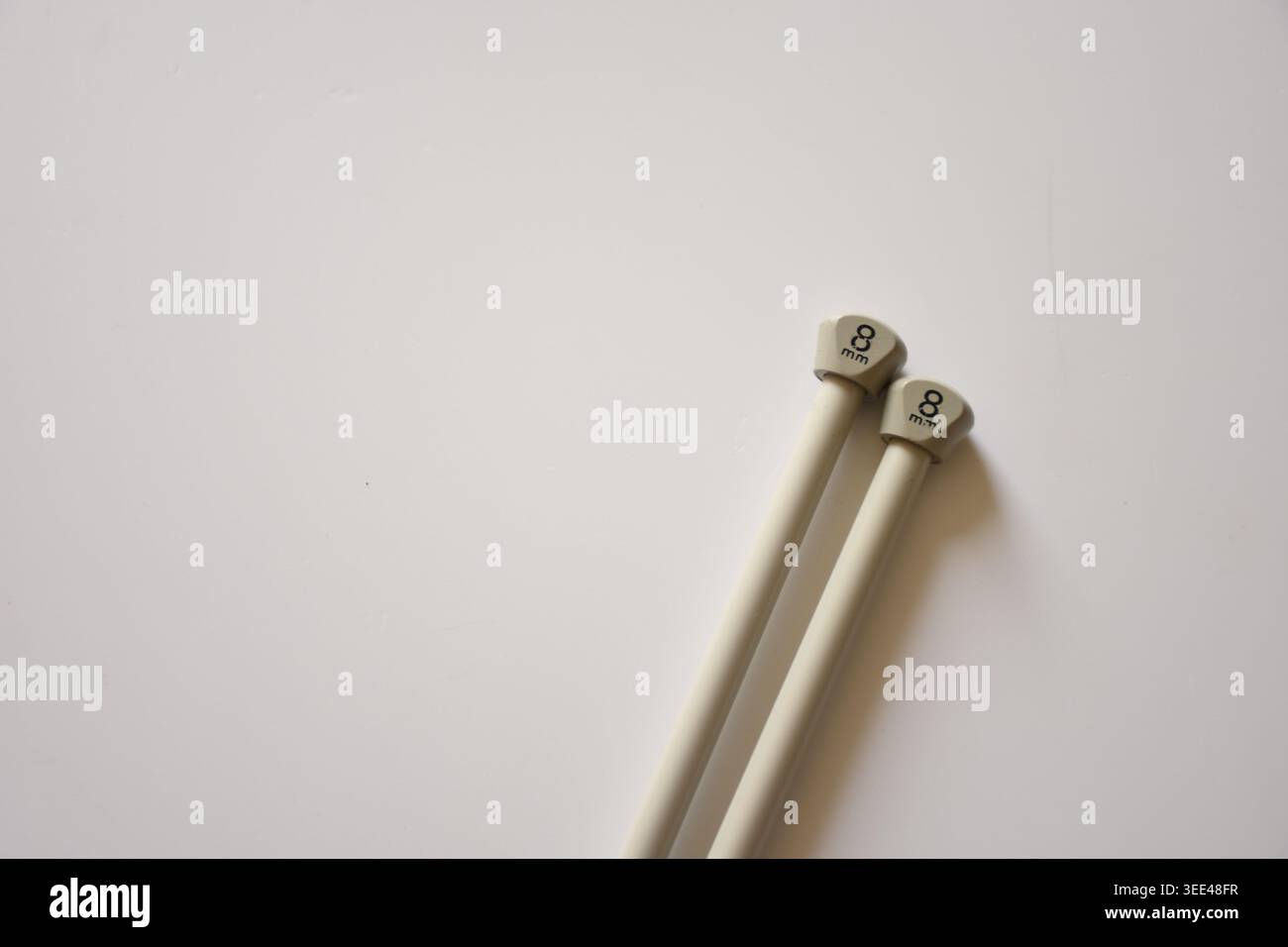 Graue Stricknadeln auf einem sauberen weißen Tisch mit minimalistischer Zusammensetzung und sanfter natürlicher Beleuchtung. Perfekt für Strickkonzepte, Stockfoto