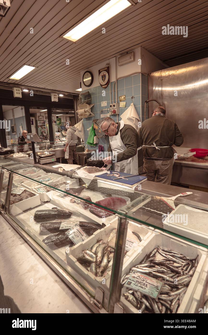 Zwei erfahrene Fischhändler bereiten aktiv frischen Fisch hinter einer gut sortierten Verkaufstheke an einem belebten Marktstand in Florenz, Italien, zu. Die Stockfoto