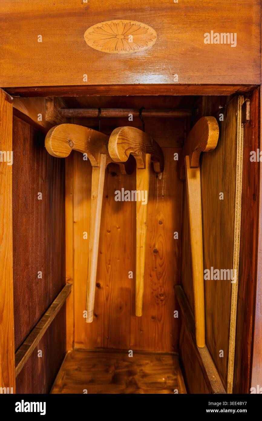 Drei rustikale Holzschuhtragen hängen in einem alten Holzschrank mit einem kunstvoll geschnitzten Design auf der oberen Platte. Die Elemente sind beleuchtet Stockfoto