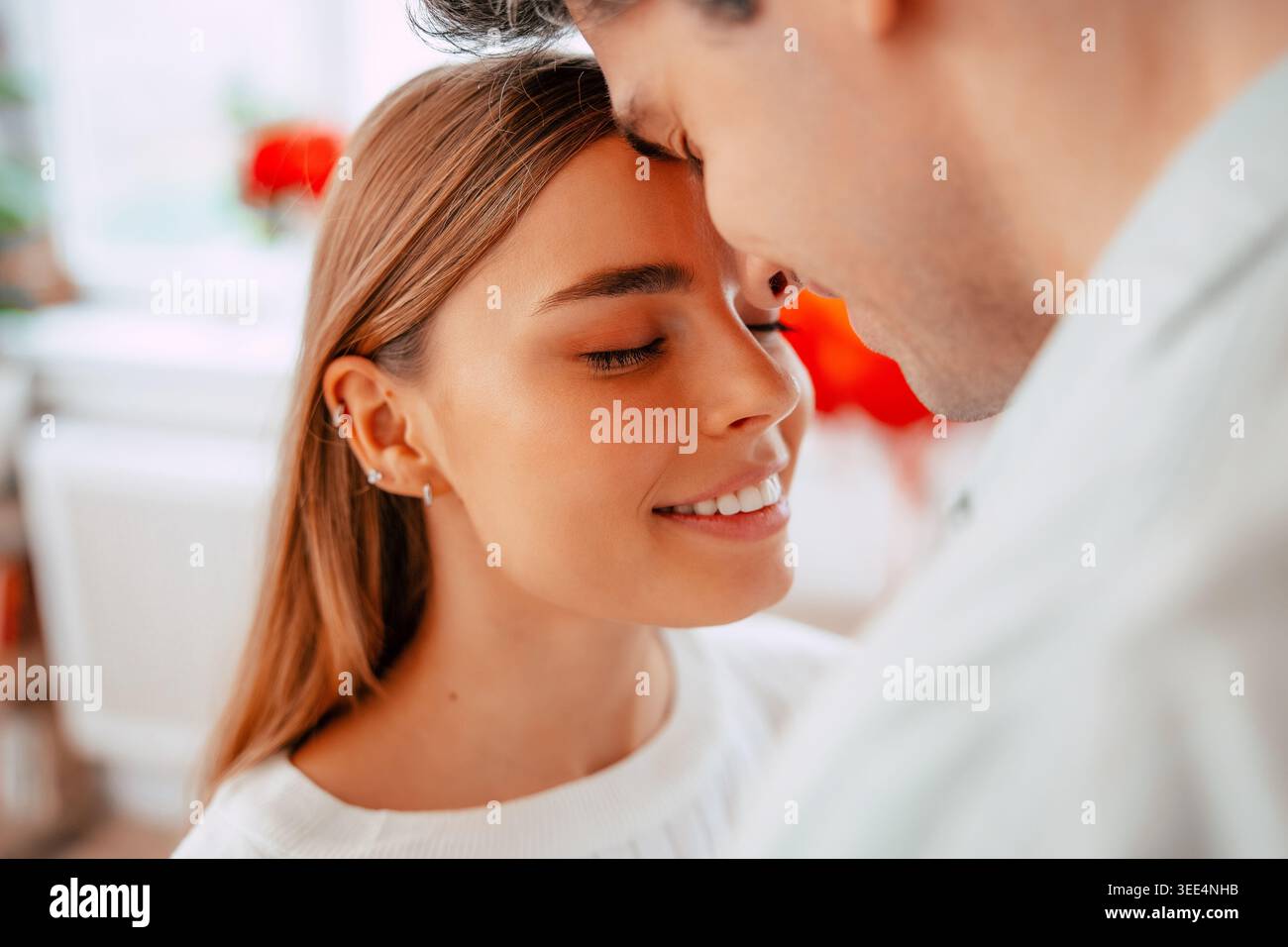 Romantisches junges Paar teilt zärtlichen Moment zu Hause, Mann küsst Frau auf die Stirn in einem gemütlichen modernen Wohnzimmer Stockfoto