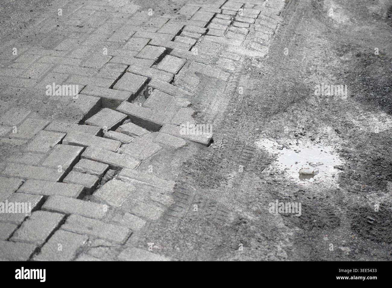 Risse im Bürgersteig und Pfützen auf einer Straße Stockfoto