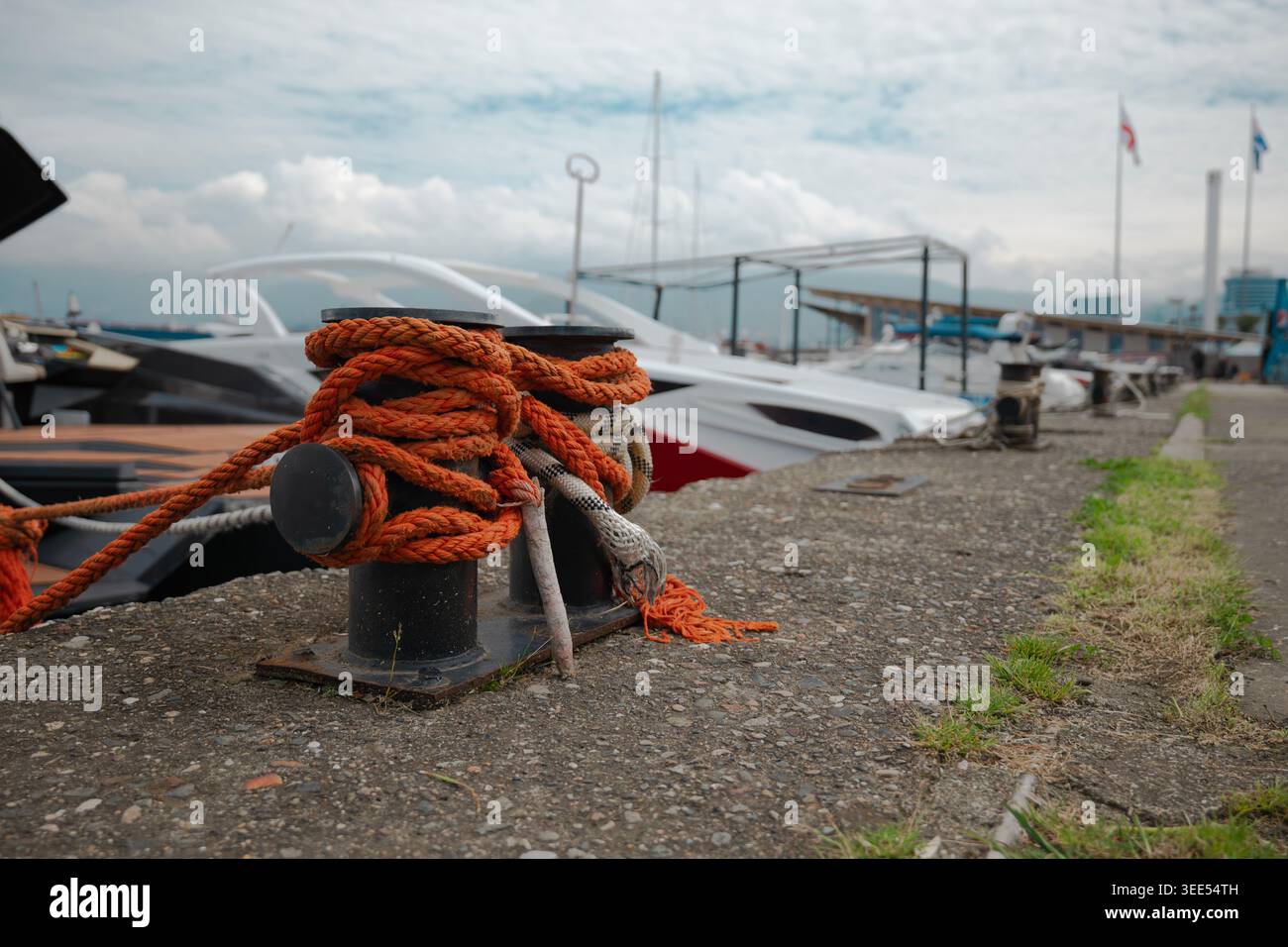 Nahaufnahme eines schwarzen Metallpfollers, gesichert mit schwerem orangenem Seil an einem kommerziellen Bootsanleger Stockfoto