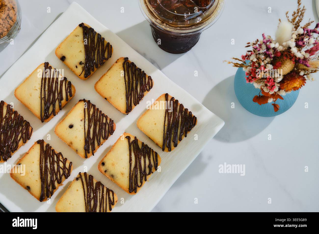 Viele quadratische Muffins mit Schokoladensoße auf weißem Teller serviert mit Eiskaffee. Stockfoto