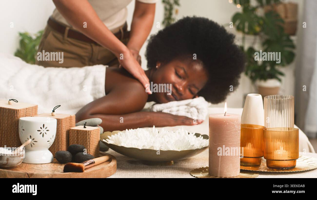 Entspannende Spa-Massage Für Frauen Mit Afro-Frisur, Umgeben Von Kerzen Und Aromatherapie-Dekor Stockfoto