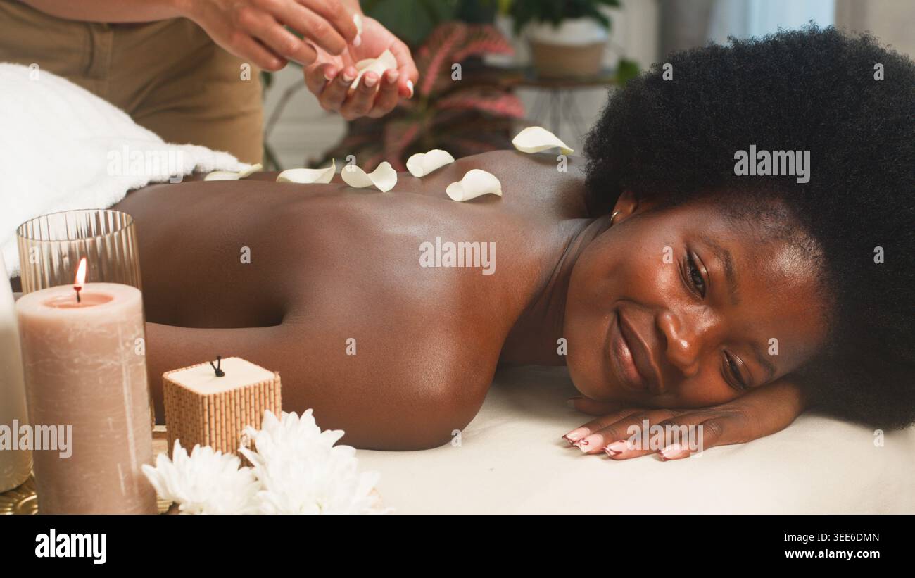 Entspannende Spa-Massage mit Rosenblüten und Kerzen - Frau genießt Aromatherapie-Behandlung Stockfoto