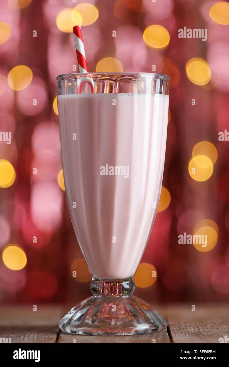 Erdbeeren-Milchshake mit gestreiftem rotem Stroh in hohem Glas, der auf einem Holztisch mit funkelnden Bokeh-Lichtern sitzt Stockfoto