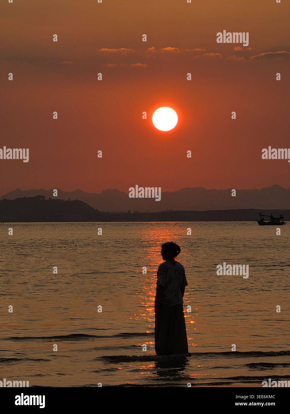 Silhouette einer Person, die im Wasser steht und den hellen orangefarbenen Sonnenuntergang über dem Ozean beobachtet und sich friedlich und friedlich anfühlt Natur Schönheit ruhige Meer dista zu betrachten Stockfoto