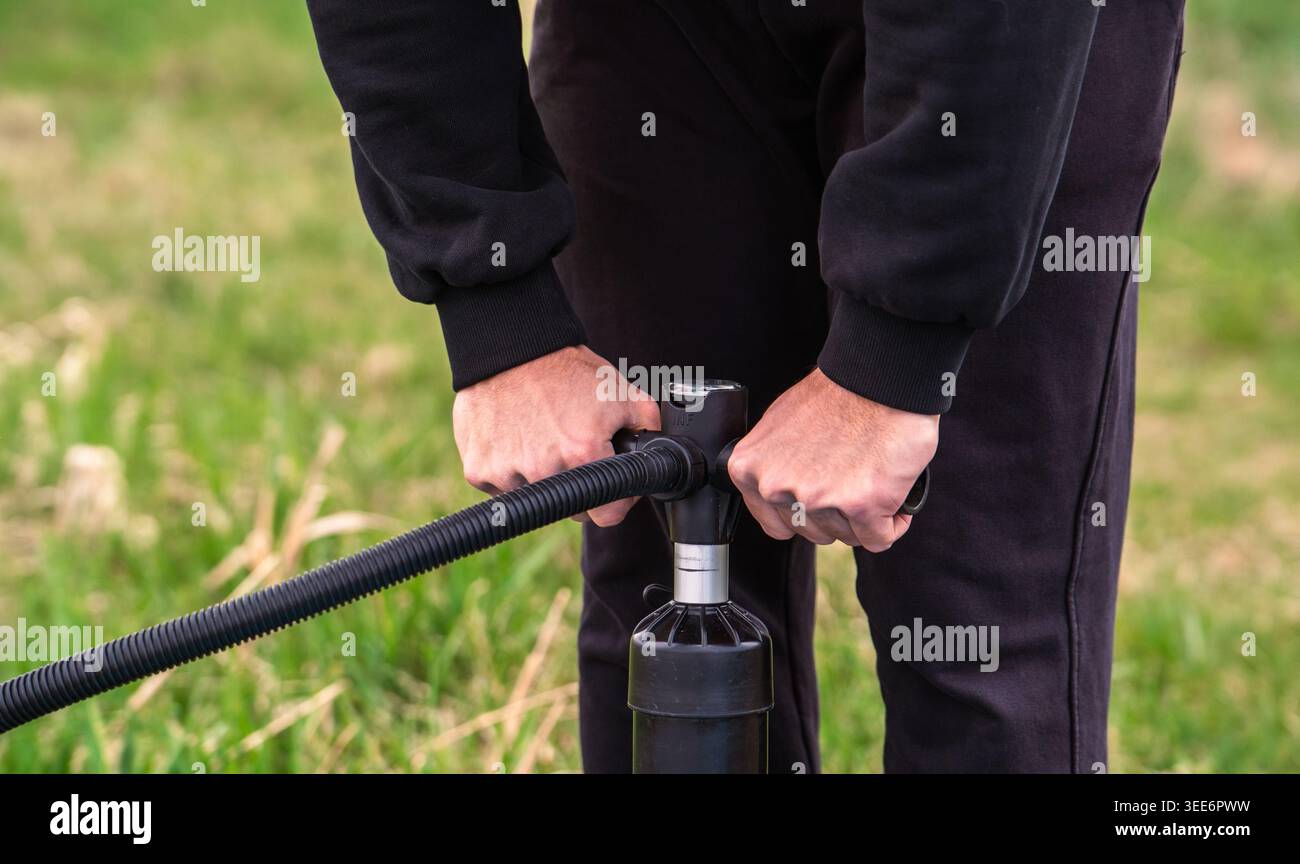Mittelteil einer Person, die Ausrüstung mit einer Handpumpe im Freien aufpumpt Stockfoto