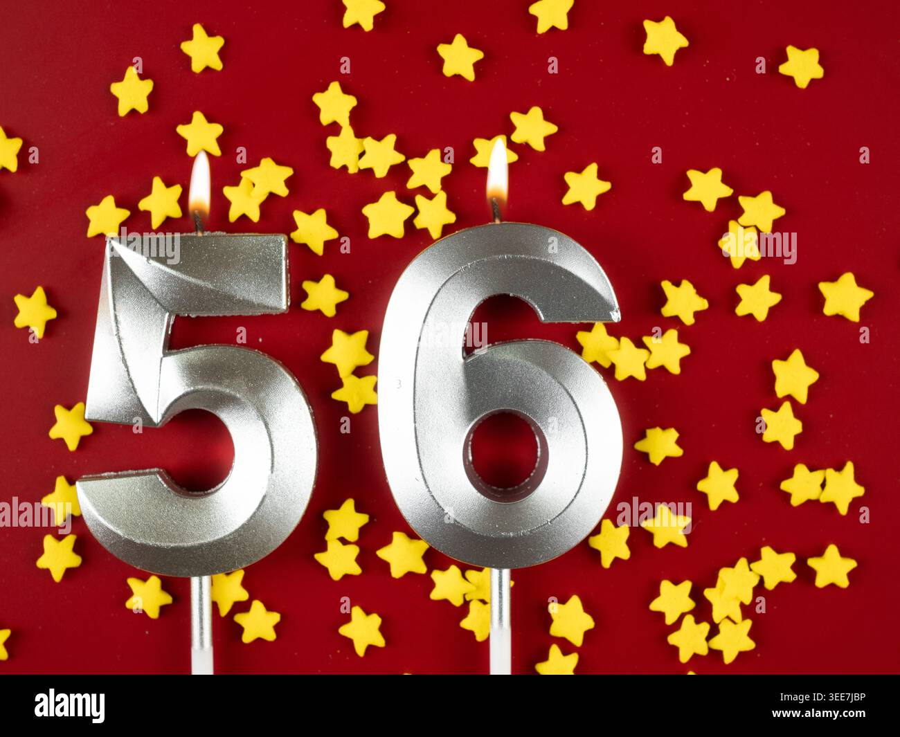 Nummer 56 silberne Geburtstagskerze auf rotem Hintergrund mit goldenen Sternen. Sechsundfünfzigjähriger Geburtstag. Konzept der Feier von Jubiläum und bir Stockfoto