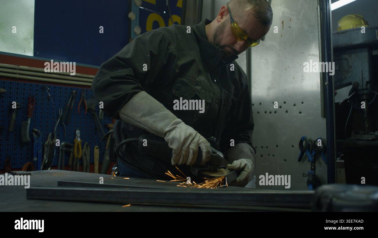 Geschulter Handarbeiter mit Schutzausrüstung zum Schleifen von Stahl in einer Schweißwerkstatt. Karrierekonzept in der Metallindustrie. Stockfoto