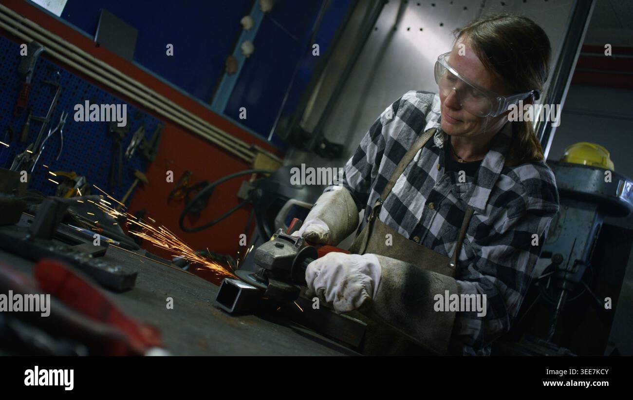 Arbeitnehmerin mit Schutzausrüstung beim Schleifen von Stahl in einer Schweißwerkstatt. Frauen in der Metallindustrie Berufskonzept. Stockfoto