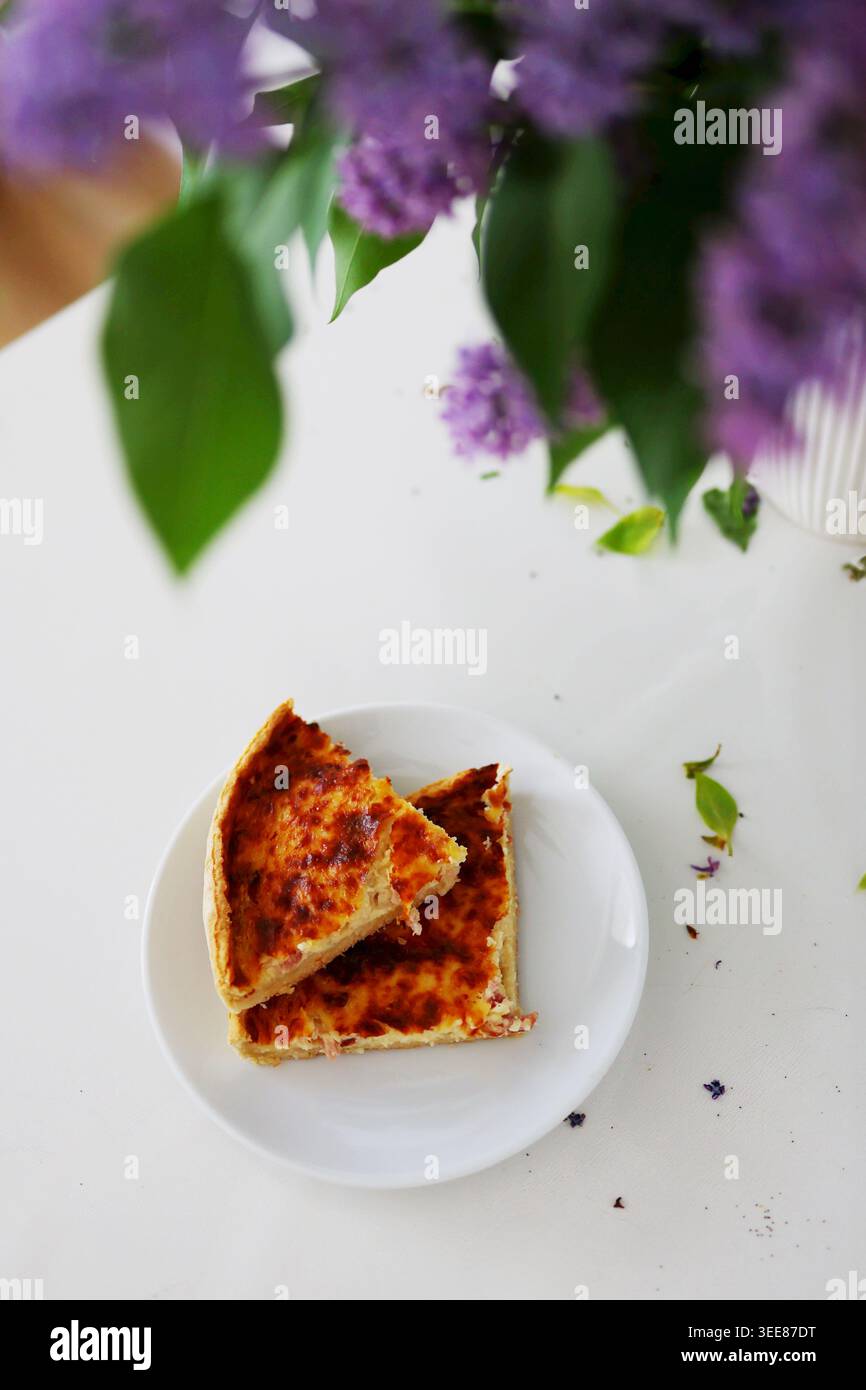 Köstlicher gebackener Kuchen in der Nähe blühender Fliederblüten in hellem, modernem Interieur mit weichem Tageslicht. Stockfoto
