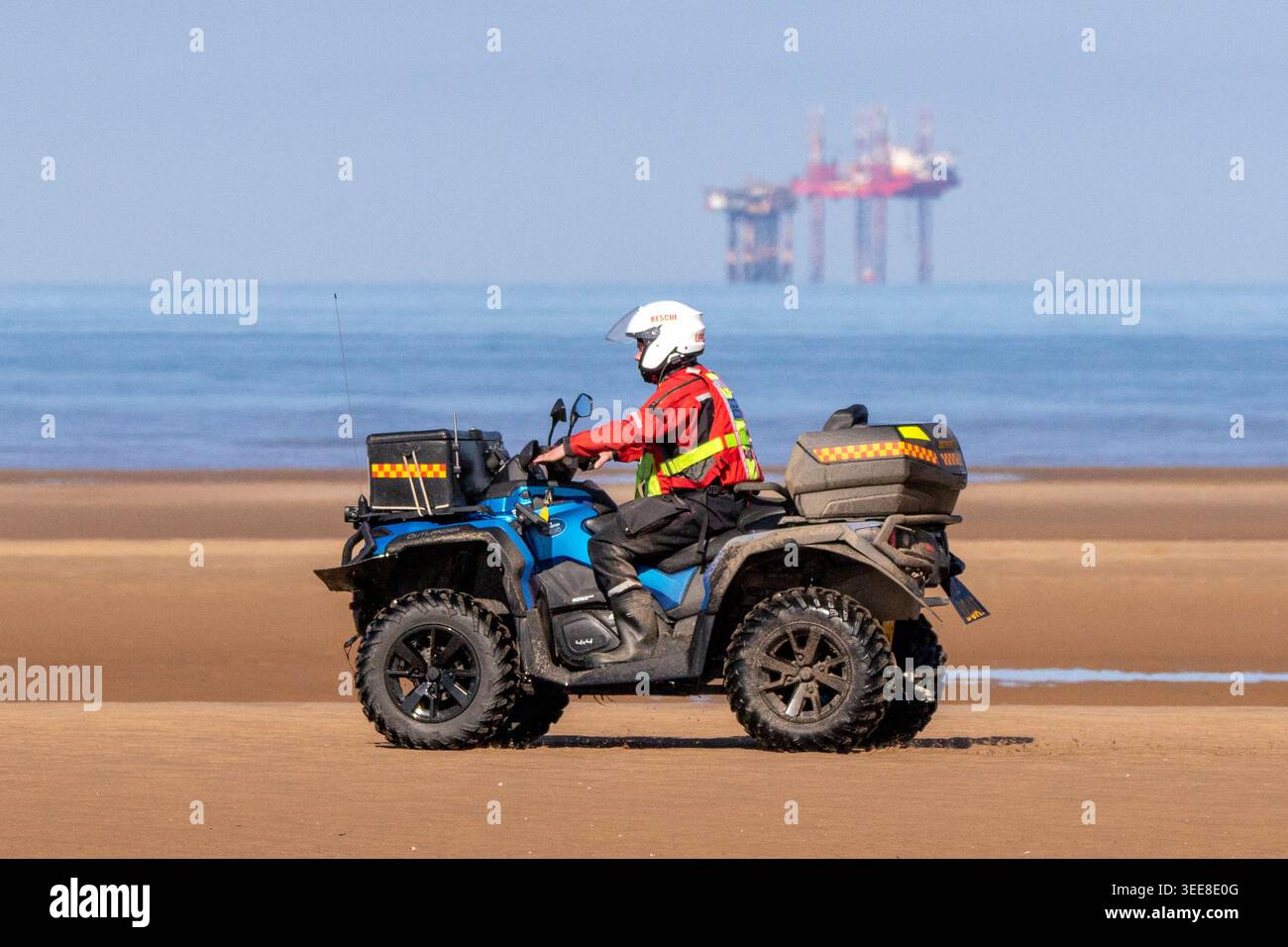 Southport Lifeboat Crew-Mitglieder, die an einem sonnigen Tag mit einem RettungsQuad über einen nassen Sandstrand fahren. Stockfoto