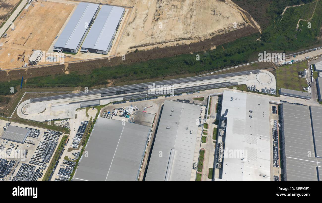Aus der Vogelperspektive des BYD Auto Thailand Fabrikkomplexes mit großen Industriegebäuden, umfangreichen Autolagerplätzen und einer Teststrecke in Phananikhom Stockfoto